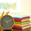 5 stacked books in different colors, pencil holder and alarm clock