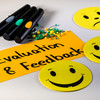 Moderationskarte mit dem Schriftzug "Evaluation & Feedback", gelbe Smilies, Stifte und Moderationsnadeln