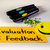 Moderationskarte mit dem Schriftzug "Evaluation & Feedback", ein gelber Smilie, Stifte und Moderationsnadeln