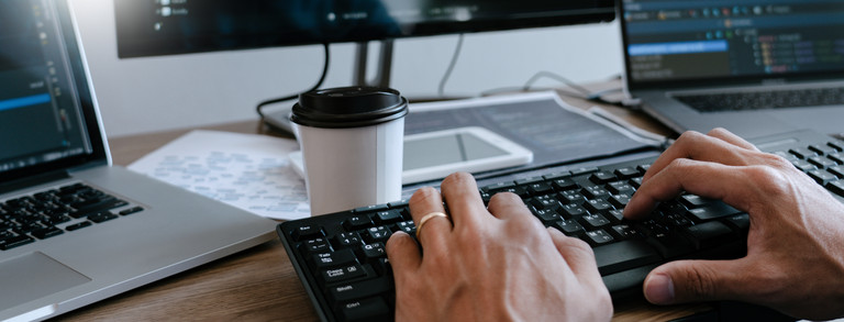 Eine Person arbeitet an einem Schreibisch mit verschiedenen Desktop-Geräten