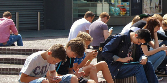 Studenten auf dem Campus schauen auf ihr Smartphone. Rechts auf dem Bild sind Icons der TU App eingeblendet.