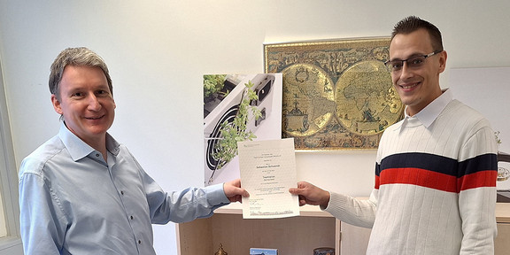 New team leader Service Desk Mr. Kötterheinrich presents Mr. Schwendt with his appointment as team leader