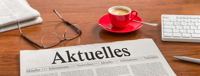 Brille, Kaffeetasse und Tageszeitung mit Titel Aktuelles auf einem Tisch