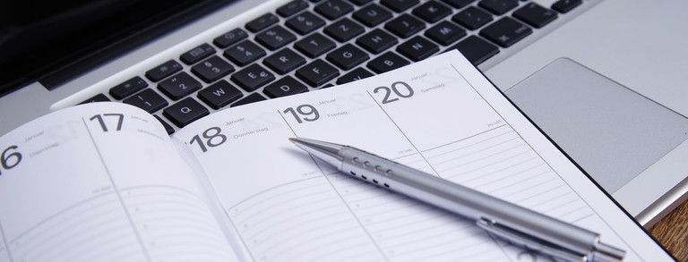 Aufgeschlagener Taschenkalender mit einem Stift auf einer Tastatur