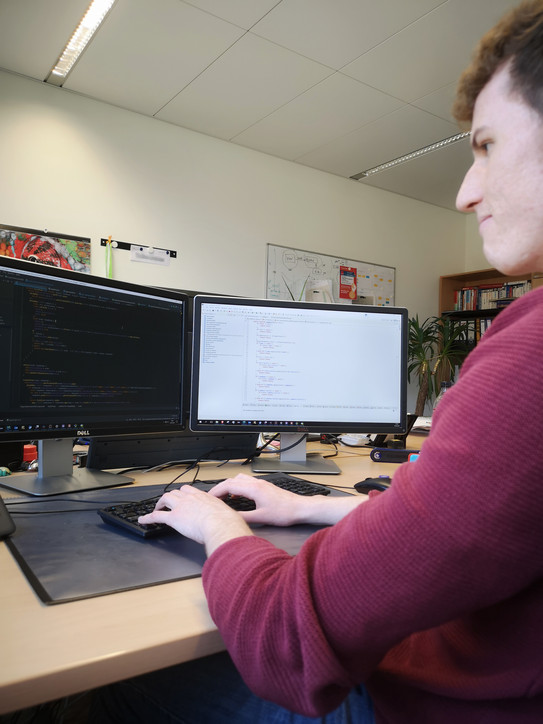 Auszubildender vor zwei Monitoren mit Quellcode