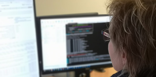 Programmiererin vor zwei Bildschirmen mit Programmiercode