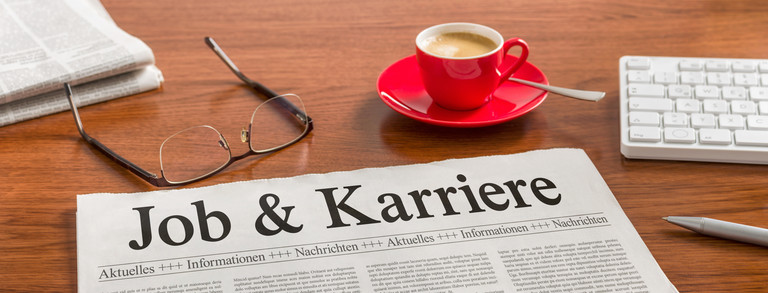 Brille, Kaffeetasse und Tageszeitung mit dem Titel "Job & Karriere" auf einem Tisch