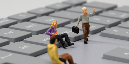 Two sitting and one running miniature human on a keyboard