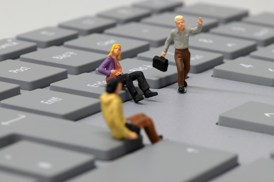 Zwei sitzende und ein laufender Miniaturmensch auf einer Tastatur