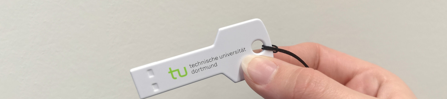 Hand hält einen Plastikschlüssel mit dem TU-Logo