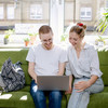 A young woman and a young man sit on a sofa and look at a laptop together.