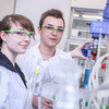 Two trainee chemical laboratory technician stands in a laboratory wearing protective clothing.