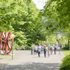 Mehrere Studierende gehen über einen Weg auf dem Campus Nord im Sommer und grüne Bäume stehen rechts und links.