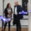 In the foreground four drones are flying, in the background two people can be seen