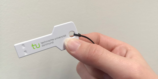 Eine Hand hält einen Plastikschlüssel mit TU-Logo