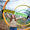 A young woman holds up a scarf with the BVB and TU Dortmund University logos in front of the spectral rings on the TU campus