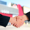 Two shaking hands. A building and a blue sky can be seen in the background.