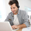 Man sits in front of the laptop and has a headset on.