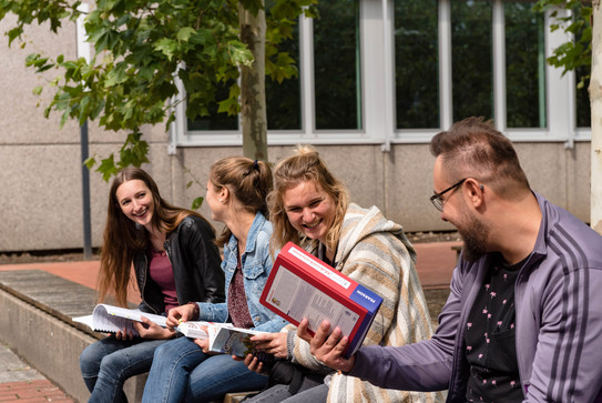 Vier Studierende sitzen auf einer Bank und unterhalten sich.